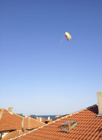 Low angle view of kite flying over building against clear blue sky