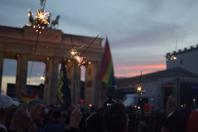 People with burning sparklers against brandenburg gate during sunset in city