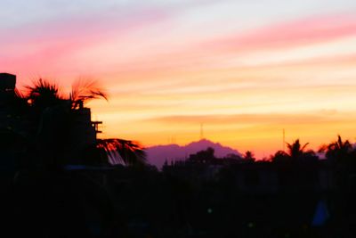Silhouette trees and cityscape against sky at sunset