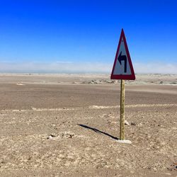 Road sign in desert against sky