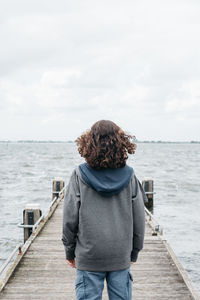 Rear view of man standing on jetty against sky