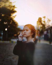 Portrait of beautiful young woman standing against sky during sunset