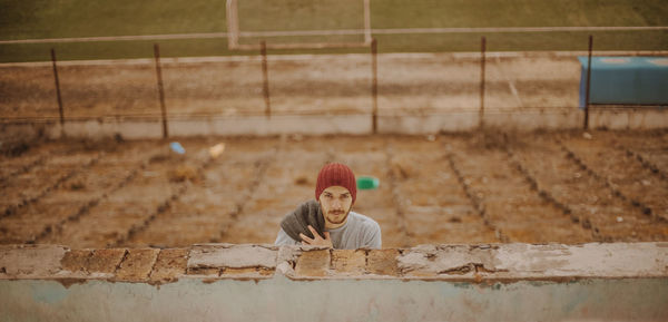 High angle portrait of young man wearing knit hat standing by brick wall