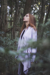Side view of thoughtful woman standing in forest