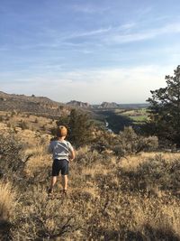 Rear view of boy standing on land against sky