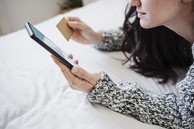 Woman with credit card doing online shopping through mobile phone while lying on bed at home