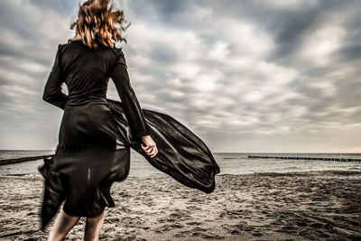 Midsection of woman at beach against sky