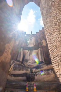 Low angle view of sunlight streaming through statue against building