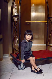 Beautiful korean girl is sitting on a clothes gurney in a hotel near the elevator