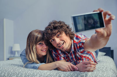 Portrait of smiling young couple taking selfie through mobile phone on bed