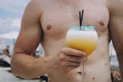 Midsection of shirtless man holding drink