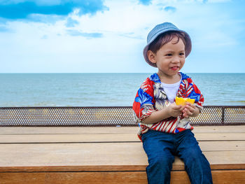 Smiling boy siting on bench against sea