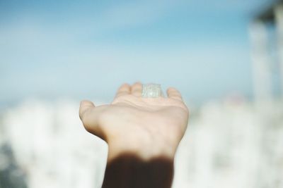 Hand of person holding cube shape against sky