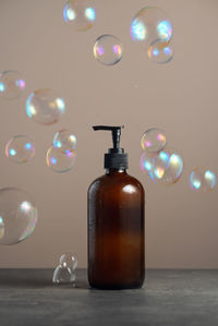 Eco-friendly glass soap dispencer with pump bottle on dark marble with soap bubles around