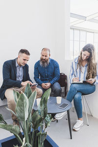 Group of busy coworkers gathering at table and working together on project in modern workspace