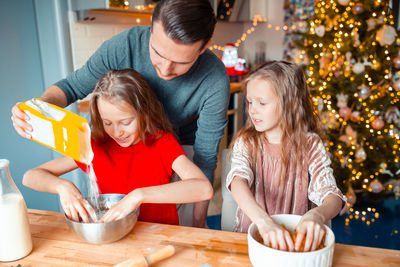 Father assisting daughters in preparing food at home during christmas