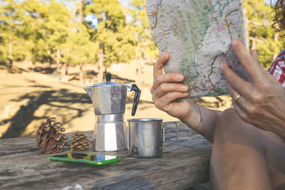 Cropped image of woman reading map while sitting in forest