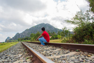 Rear view of man on railroad track against sky
