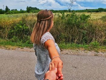 Rear view of woman holding hand on road amidst field