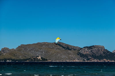 Scenic view of sea against clear blue sky with kite surfer in foreground