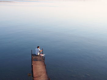High angle view of man sitting on bridge by sea