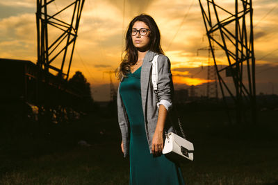 Portrait of young woman standing against sky during sunset