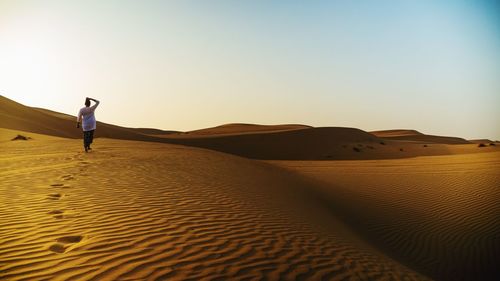 Human on sand dune in desert against blue sky 
