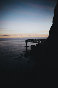 Silhouette bridge over sea against sky during sunset