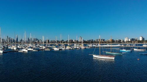 Sailboats moored in harbor against clear blue sky