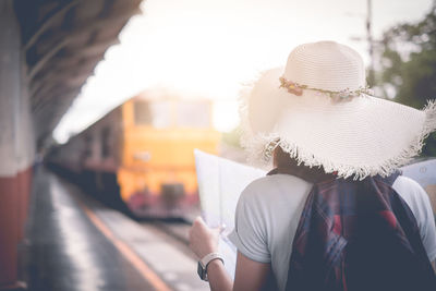 Rear view of woman holding map while standing at railroad station platform in city