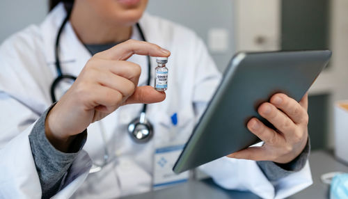 Midsection of doctor holding vaccine using digital tablet