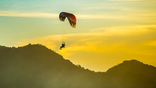 Silhouette person paragliding against mountains and sky during sunset