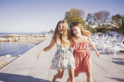 Friends enjoying while walking on sidewalk against sea