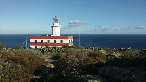 Lighthouse on beach by sea against sky