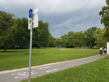 Road sign by trees against sky