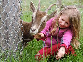 Smiling girl looking at goat while sitting on grassy land