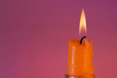 Close-up of lit candle against pink background