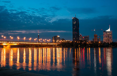 Illuminated buildings by river against sky at night