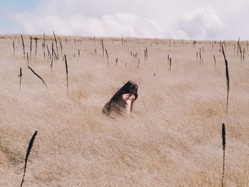 Rear view of shirtless woman sitting amidst plants on field