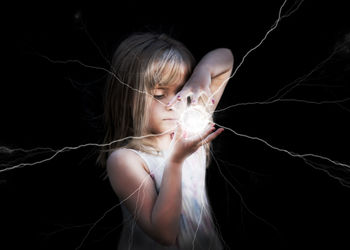 Digital composite image of cute girl holding fireball against black background