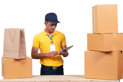 Delivery man using digital tablet by cardboard boxes against white background