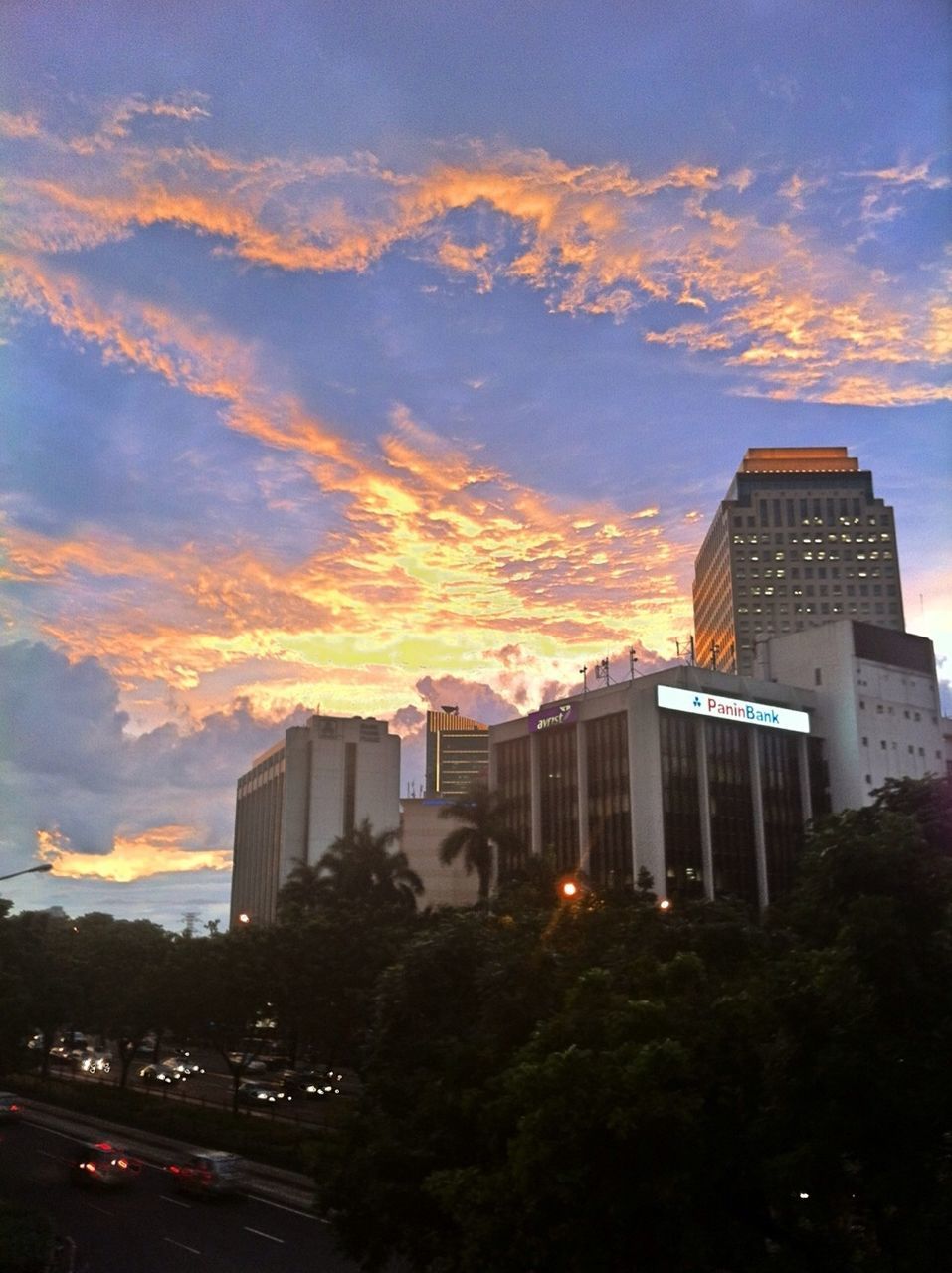 building exterior, architecture, built structure, sunset, sky, city, cloud - sky, tree, silhouette, car, orange color, transportation, cloud, city life, dusk, road, building, land vehicle, outdoors, cloudy