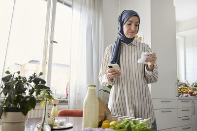 Woman in headscarf unpacking groceries at home and checking receipt