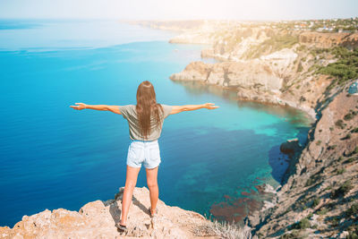 Rear view of woman standing on rock by sea