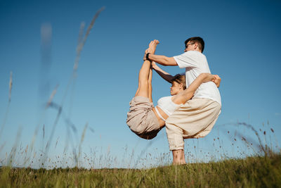 Man and woman dressed alike doing difficult pose while practicing yoga outdoors in the field