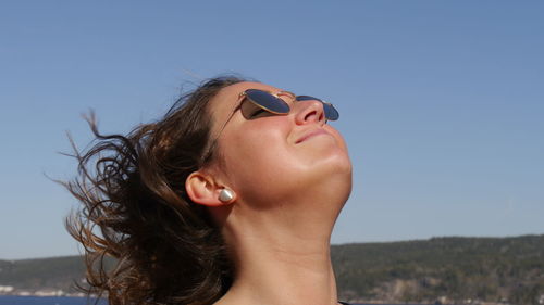 Beautiful young woman wearing sunglasses against clear sky