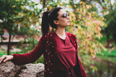 Young woman looking away while standing against trees