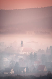 Buildings against sky during sunset and fog 