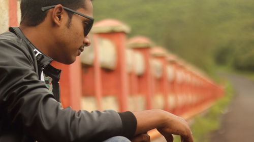 Side view of young man wearing sunglasses while sitting on bridge