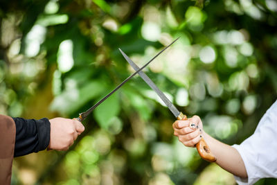 Cropped image of women holding swords against blurred background